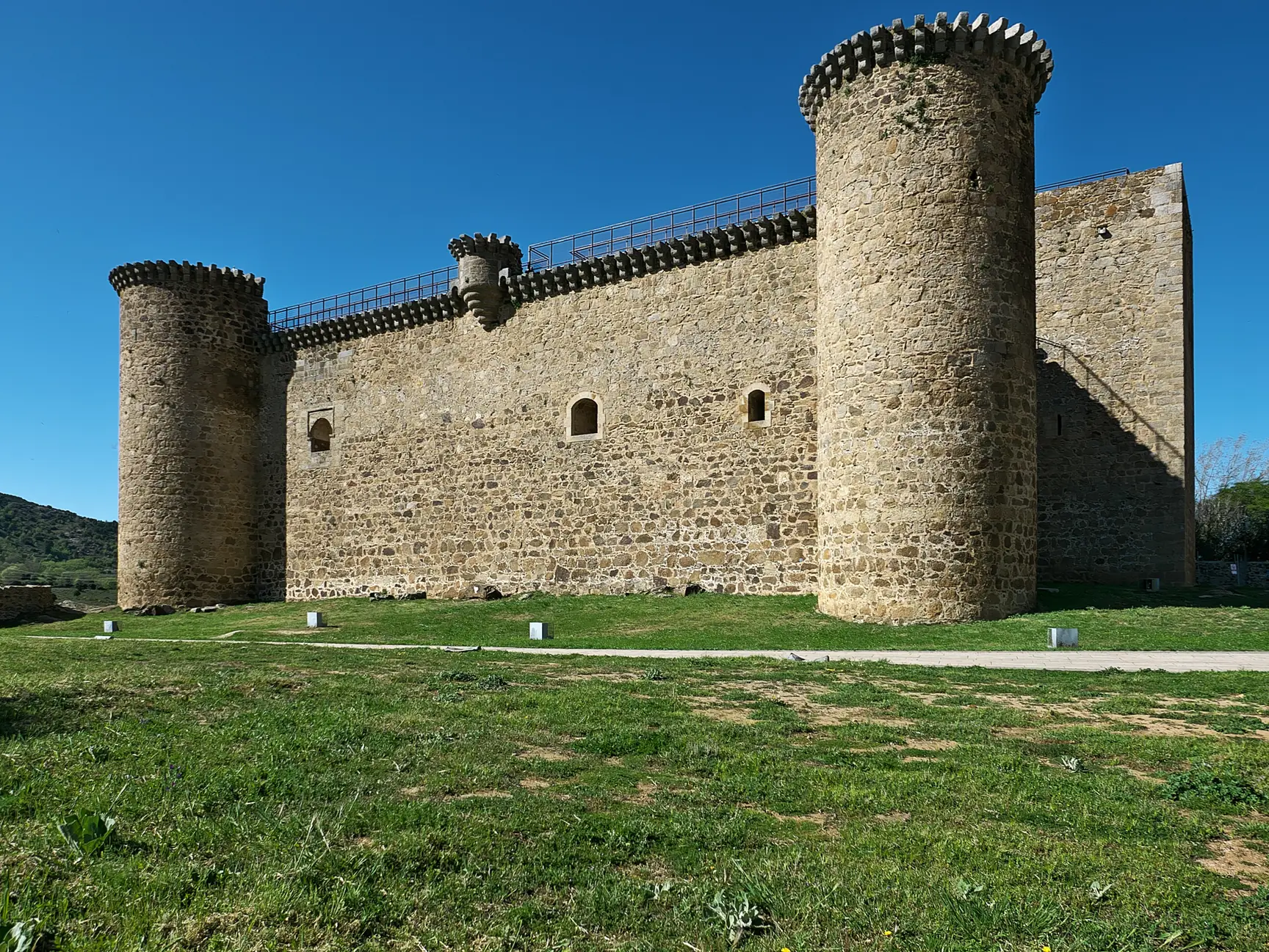 Castillo de Valdecorneja en El Barco de Ávila, con muros de piedra y torres cilíndricas sobre la pradera verde