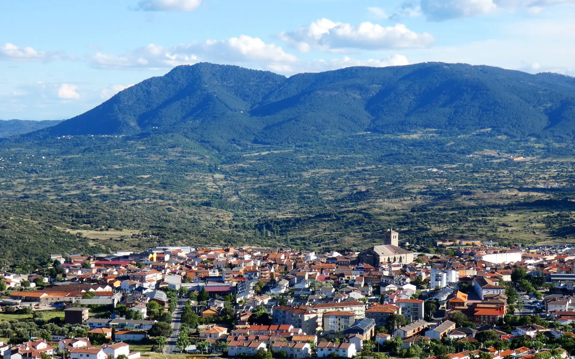 Vista elevada de Cebreros con sus tejados rojizos y la torre de la iglesia, y detrás el valle cubierto de monte y la sierra verde de Guisando