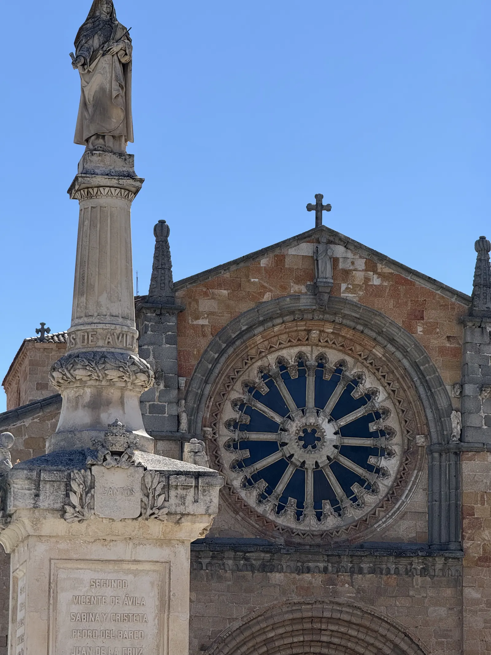 Rosetón de San Pedro de Ávila tras la columna con la estatua de Santa Teresa y los santos de Ávila en el pedestal. Foto propia La Maleta Inquieta, septiembre 2026.