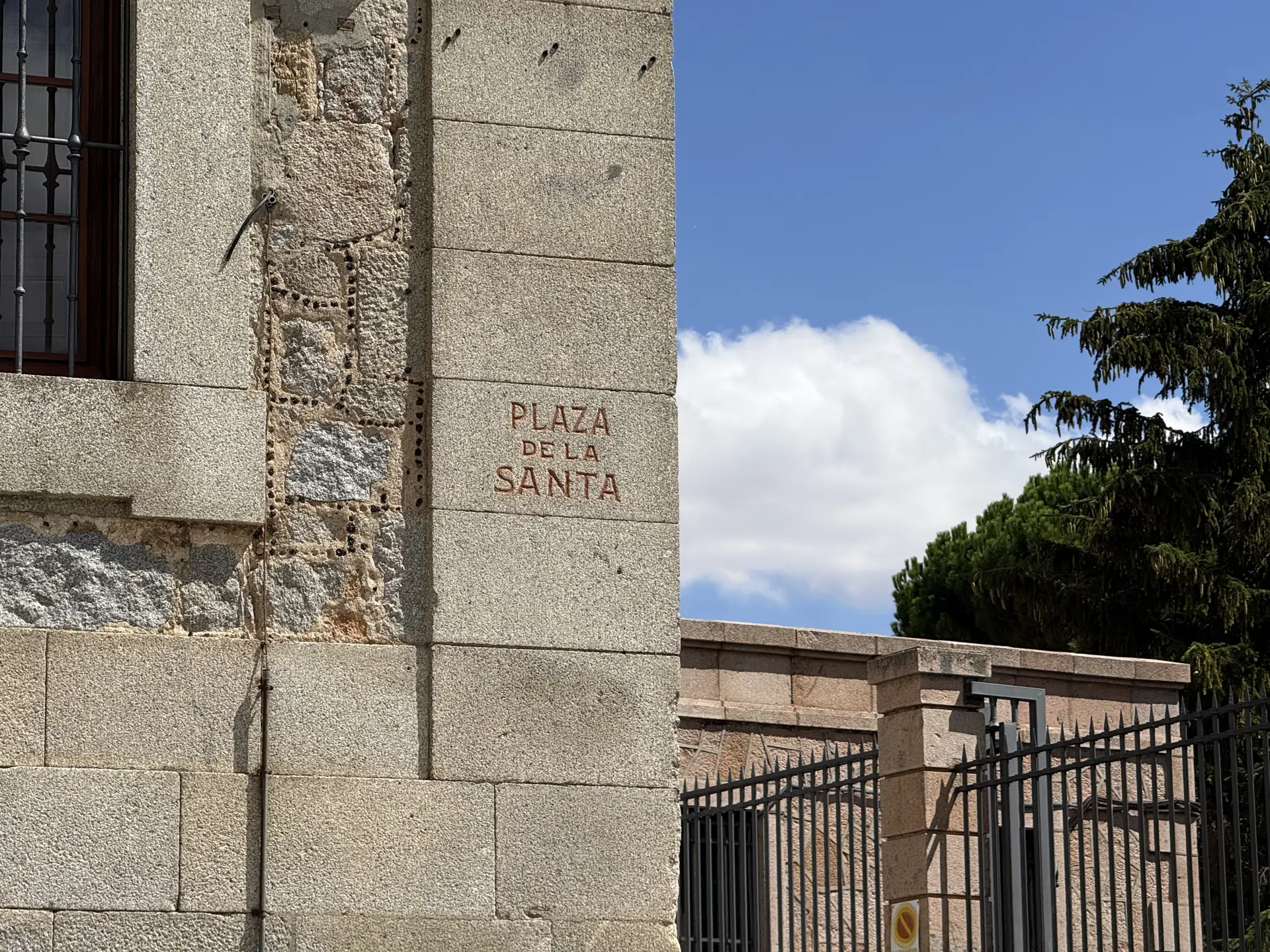 Nombre Plaza de la Santa grabado en rojo en la esquina de granito de un edificio de Ávila, junto a una verja. Foto propia La Maleta Inquieta, septiembre 2026.