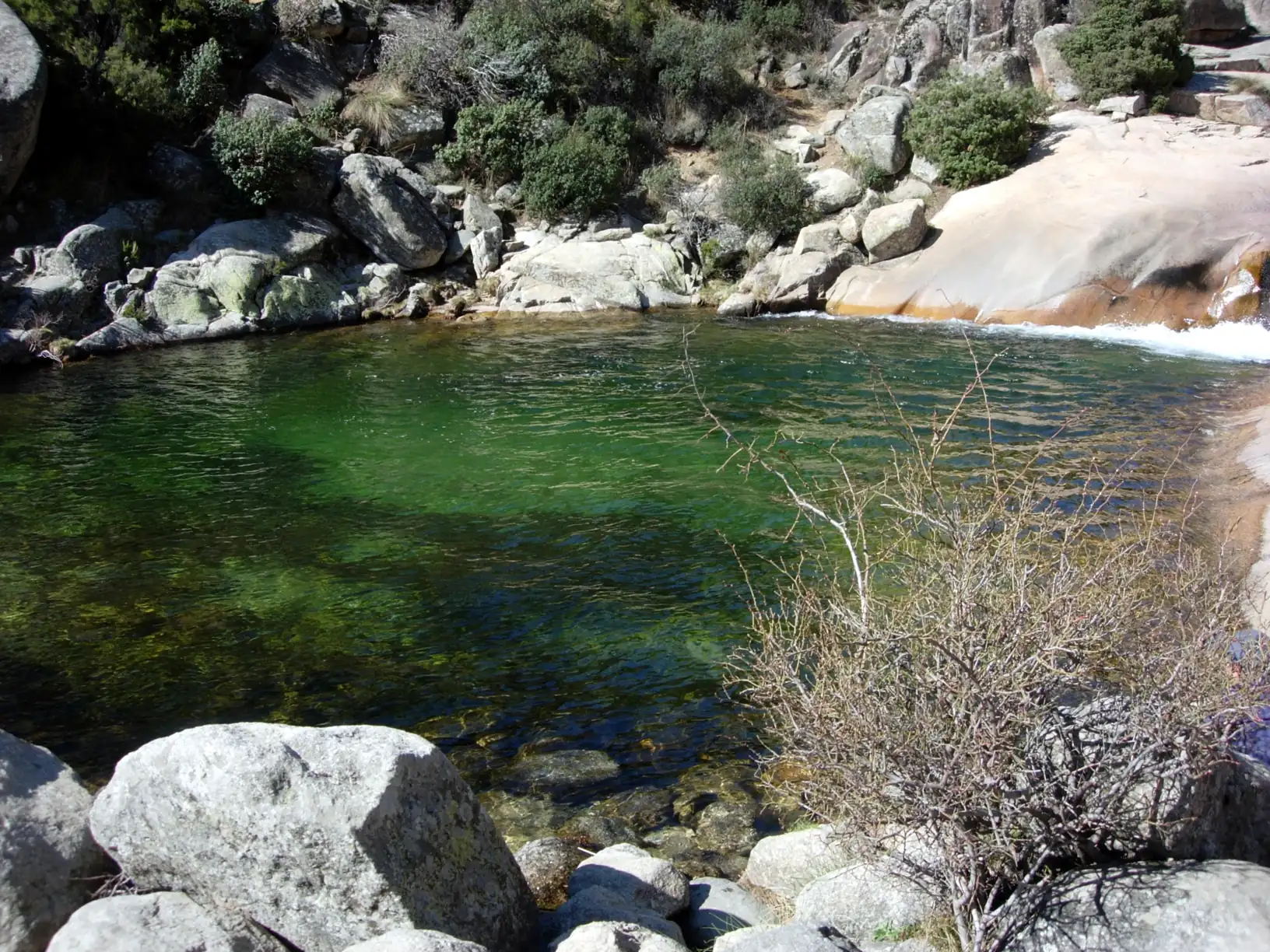 Poza de agua verde y transparente de la Charca Verde entre rocas de granito en La Pedriza
