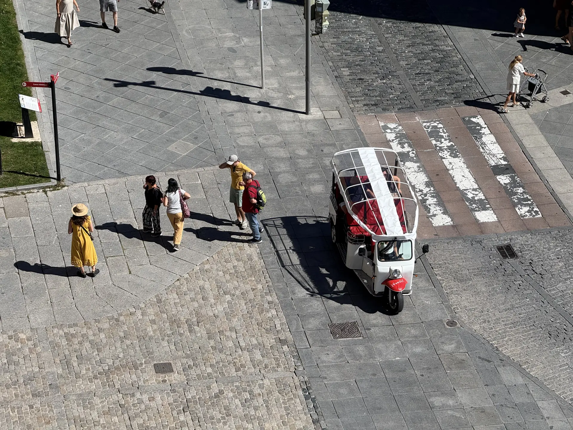 Tuk-tuk turístico junto a un paso de cebra al pie de la muralla de Ávila, visto en picado desde el adarve. Foto propia La Maleta Inquieta, septiembre 2026.
