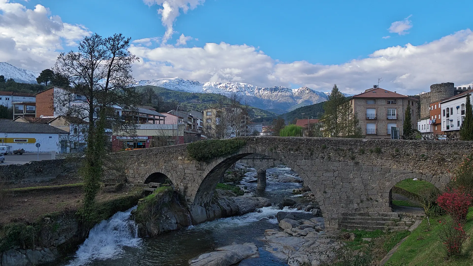 Puente medieval de piedra de Aquelcabo sobre el río Arenal en Arenas de San Pedro, con el pueblo, la torre del castillo y Gredos nevado al fondo