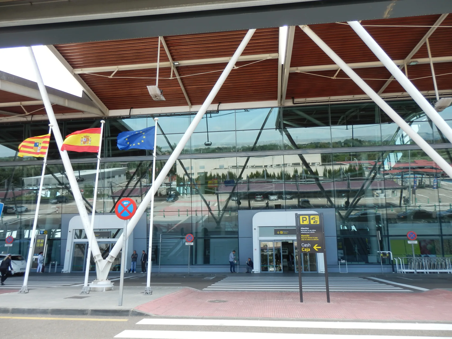 Entrada de la terminal del aeropuerto de Zaragoza, fachada de cristal bajo la cubierta de madera y la bandera de Aragón