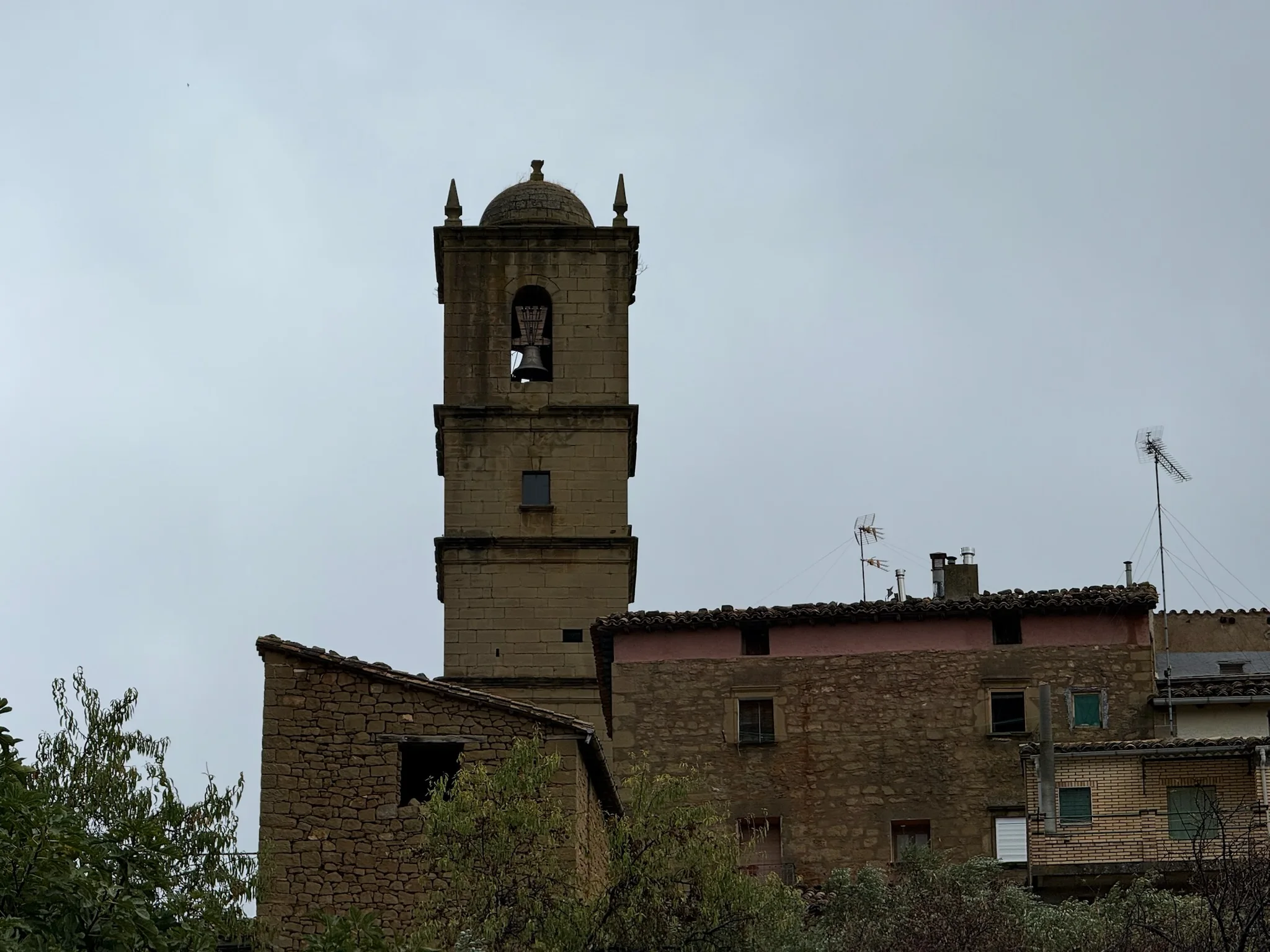 Campanario de piedra de la iglesia de Agüero con casas del pueblo y cielo nublado. Foto propia La Maleta Inquieta, octubre 2026