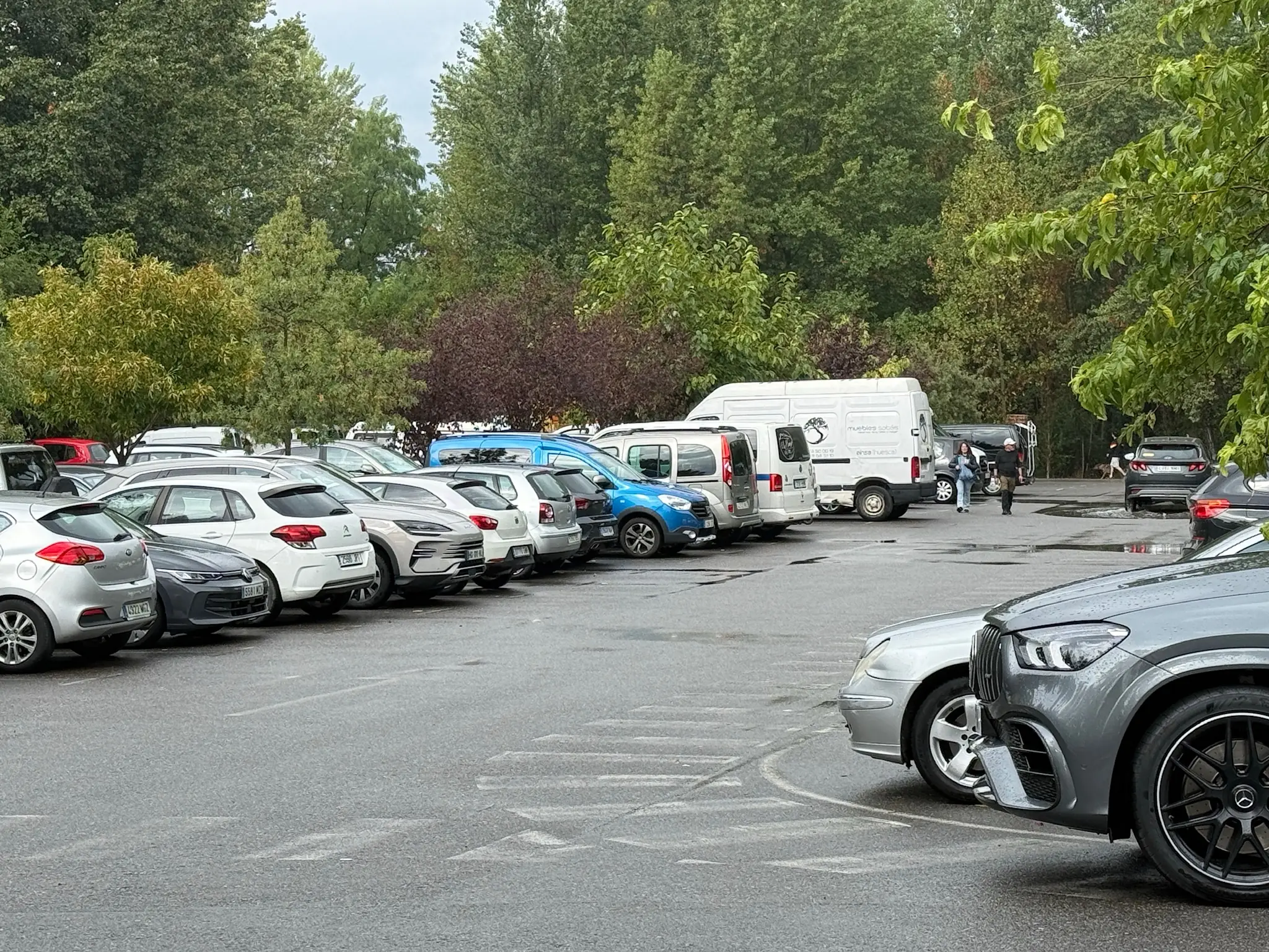 Aparcamiento público de Aínsa con coches y furgonetas estacionados entre árboles. Foto propia La Maleta Inquieta, octubre 2026