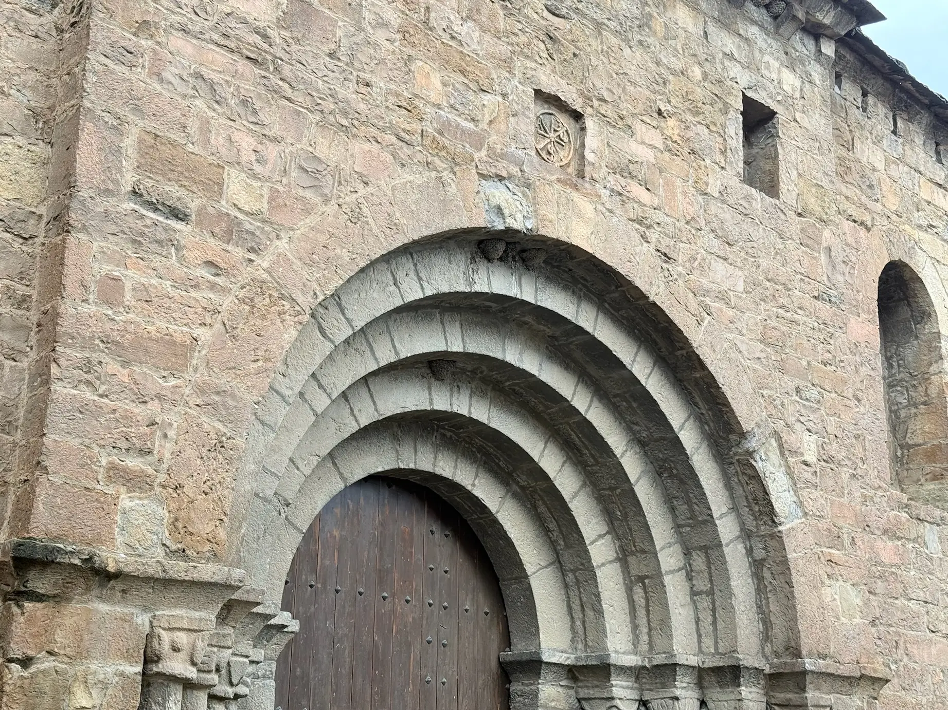 Portada románica de Santa María en Aínsa con arquivoltas concéntricas, puerta claveteada y crismón tallado encima. Foto propia La Maleta Inquieta, octubre 2026