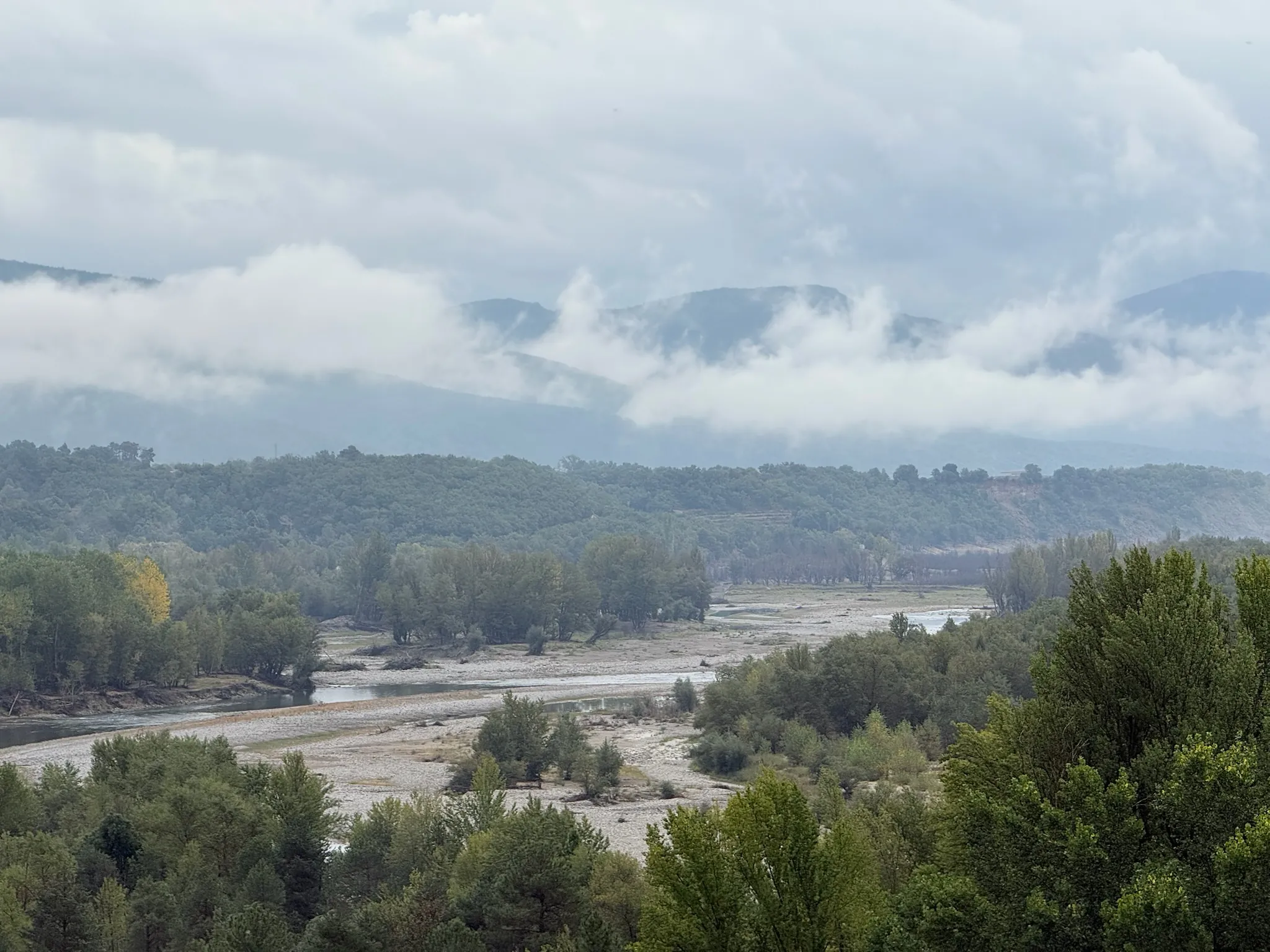 Río con cauces de grava seca, vegetación de ribera y montañas pirenaicas con nubes visto desde Aínsa. Foto propia La Maleta Inquieta, octubre 2026