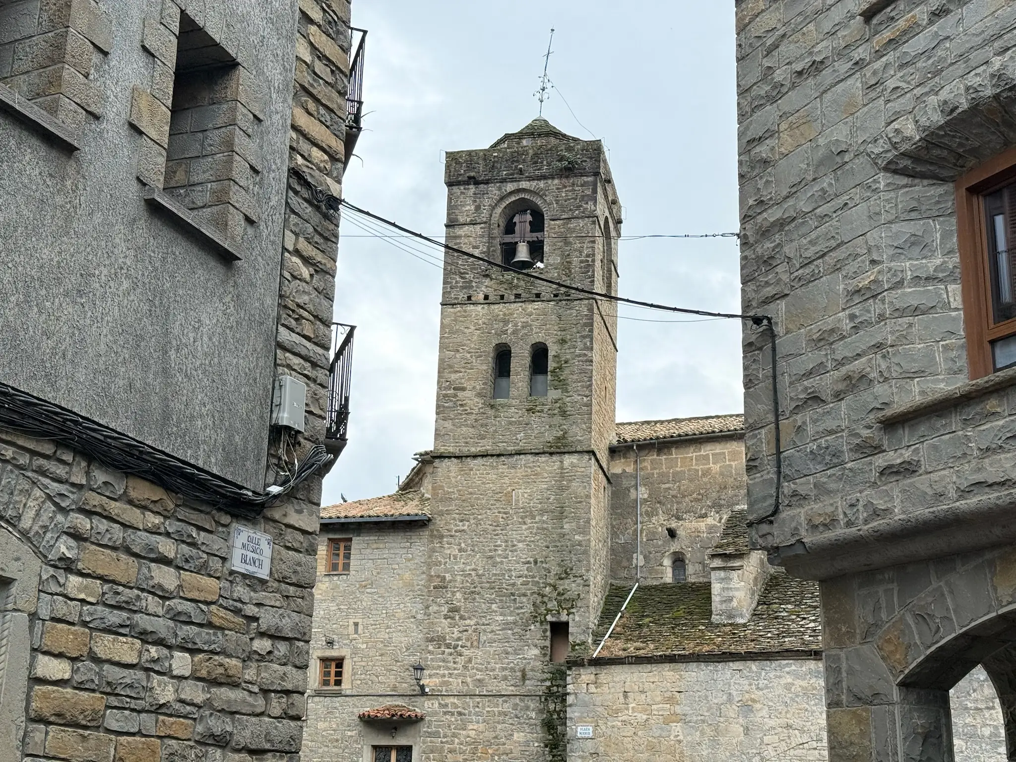 Torre de la colegiata de San Pedro de Boltaña vista entre las casas de piedra de una calle estrecha del casco antiguo. Foto propia La Maleta Inquieta, octubre 2026