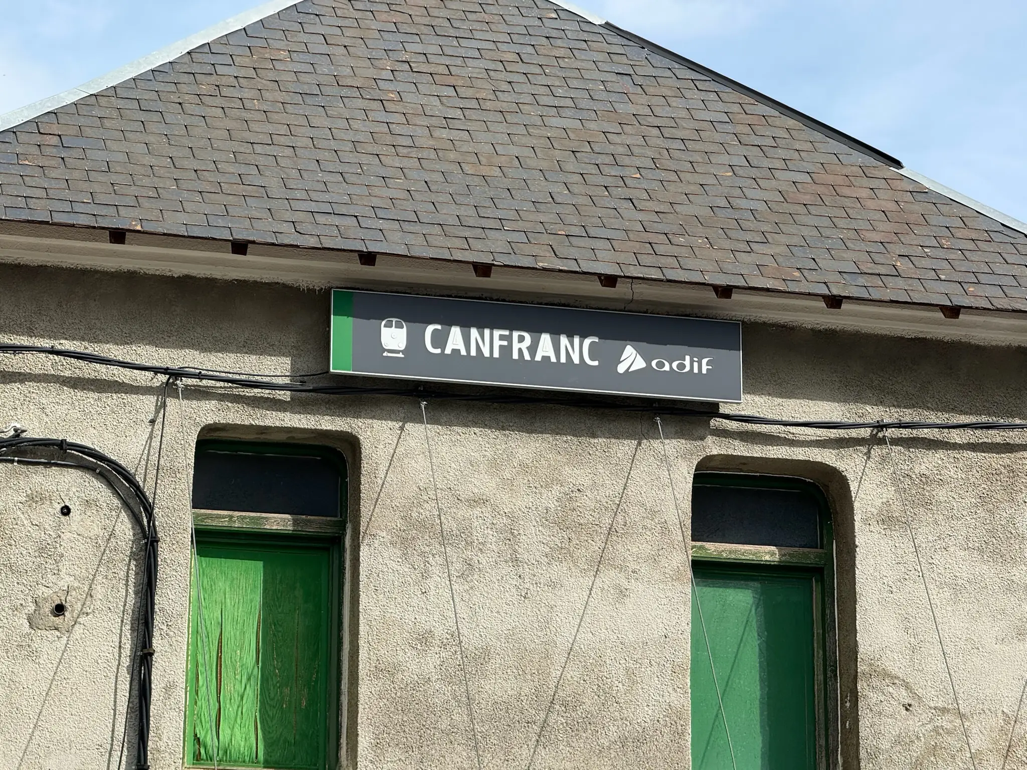 Letrero de la estación de tren de Canfranc con logo de Adif sobre fachada con puertas verdes. Foto propia La Maleta Inquieta, octubre 2026