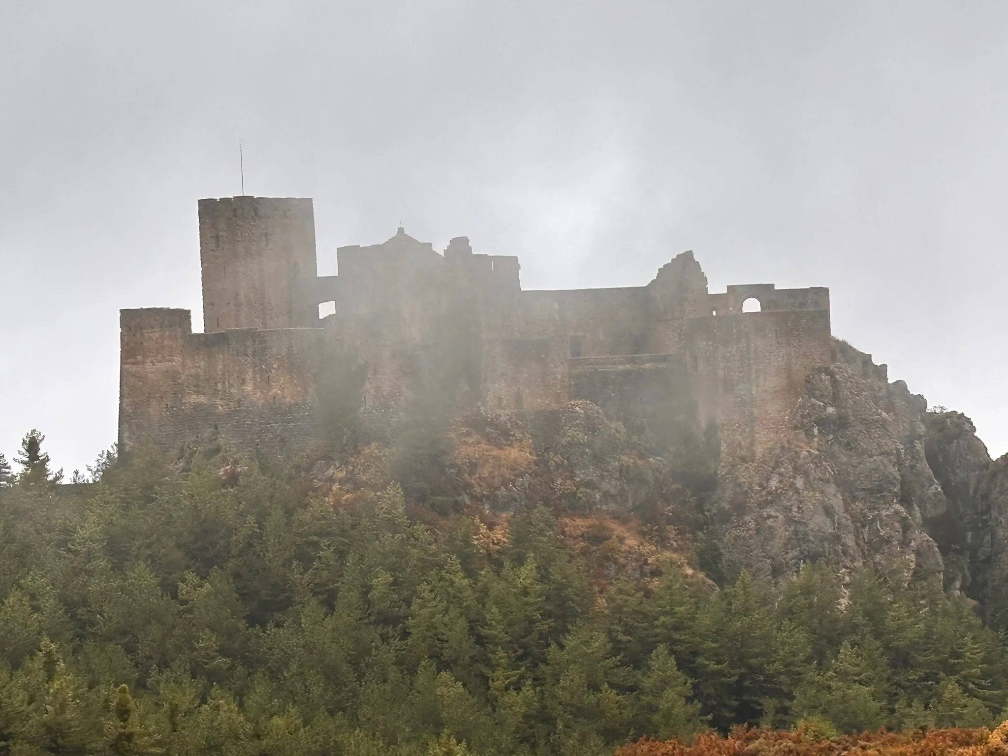 Castillo de Loarre en niebla con pinos y vegetación verde en primer plano desde el camino de acceso. Foto propia La Maleta Inquieta, octubre 2026