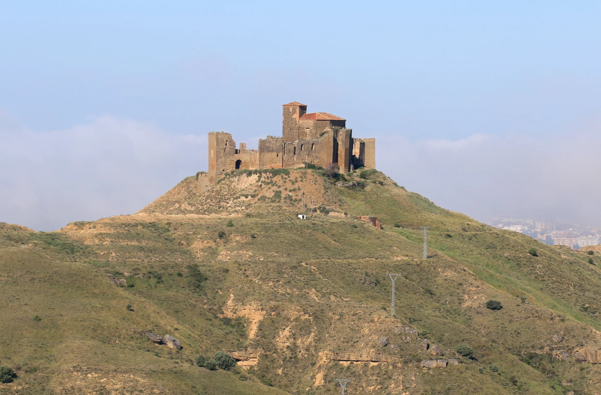 Castillo de Montearagón en lo alto de su cerro de laderas verdes, con los edificios de Huesca asomando a la derecha
