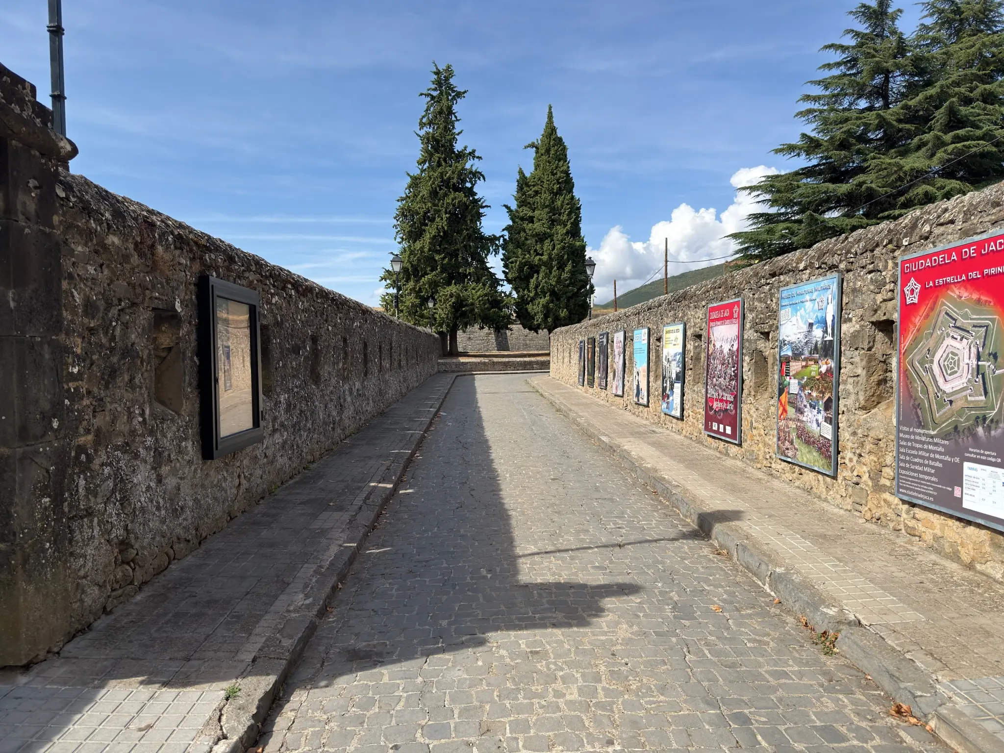 Paseo interior de la Ciudadela de Jaca con paneles informativos en el muro de piedra y árboles. Foto propia La Maleta Inquieta, octubre 2026