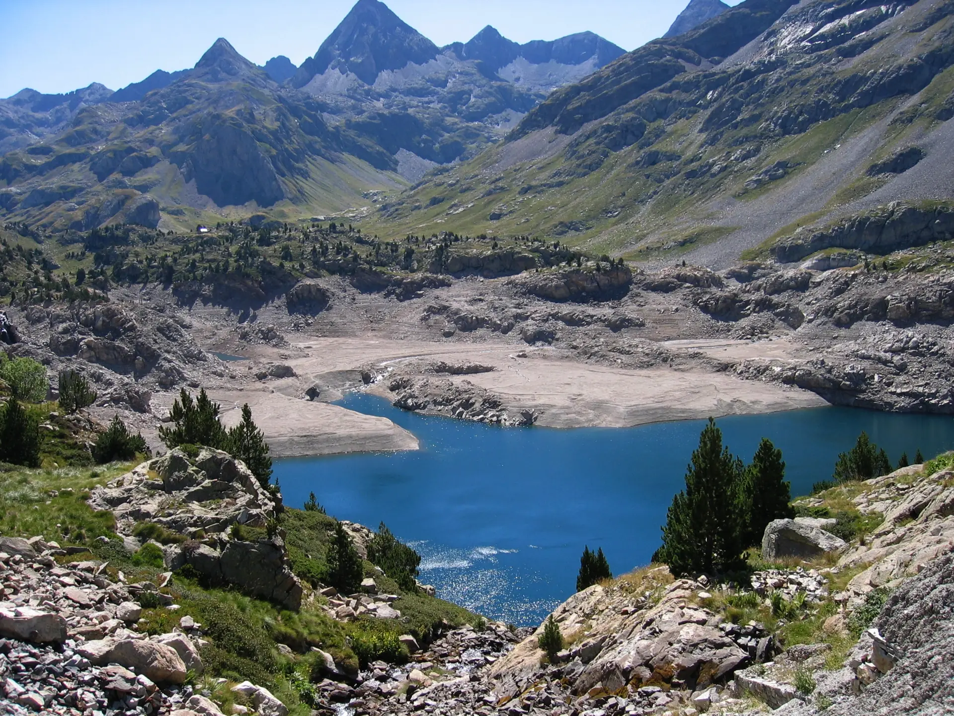 Embalse de Respomuso de aguas azules entre rocas y pinos, con los picos del Pirineo al fondo, sobre Sallent de Gállego