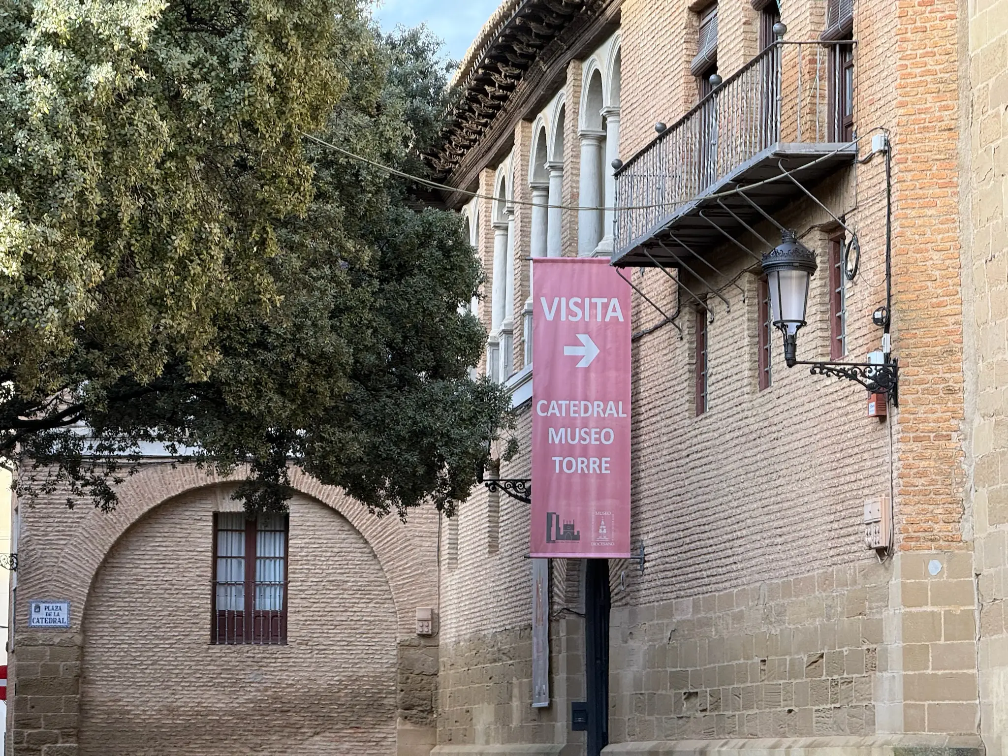 Lateral de la Catedral de Huesca con galería de arcos mudéjares y cartel rosa de acceso al museo y la torre. Foto propia La Maleta Inquieta, octubre 2026