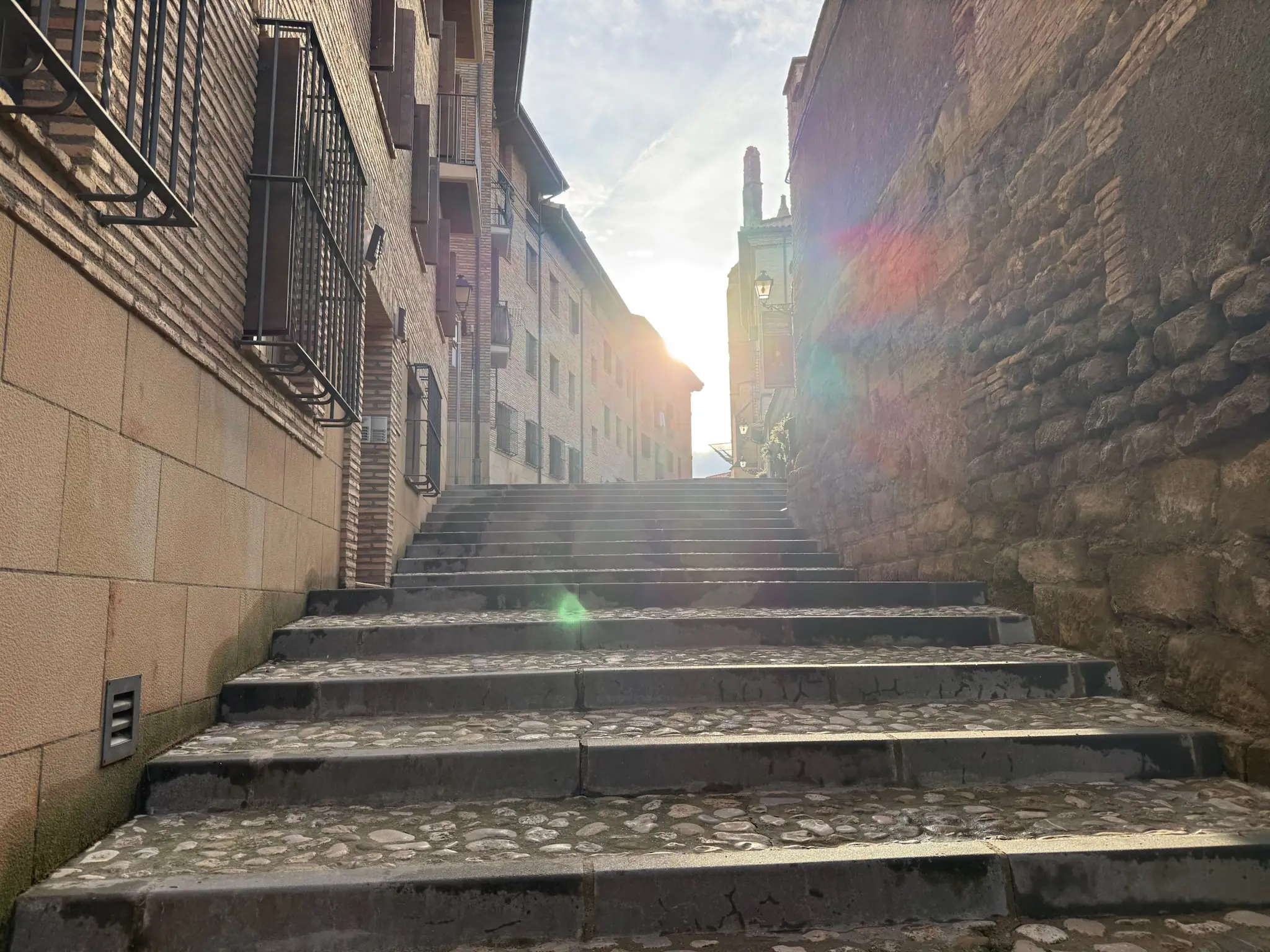 Escaleras empedradas subiendo hacia la Catedral de Huesca con torre visible al fondo y destello de sol. Foto propia La Maleta Inquieta, octubre 2026