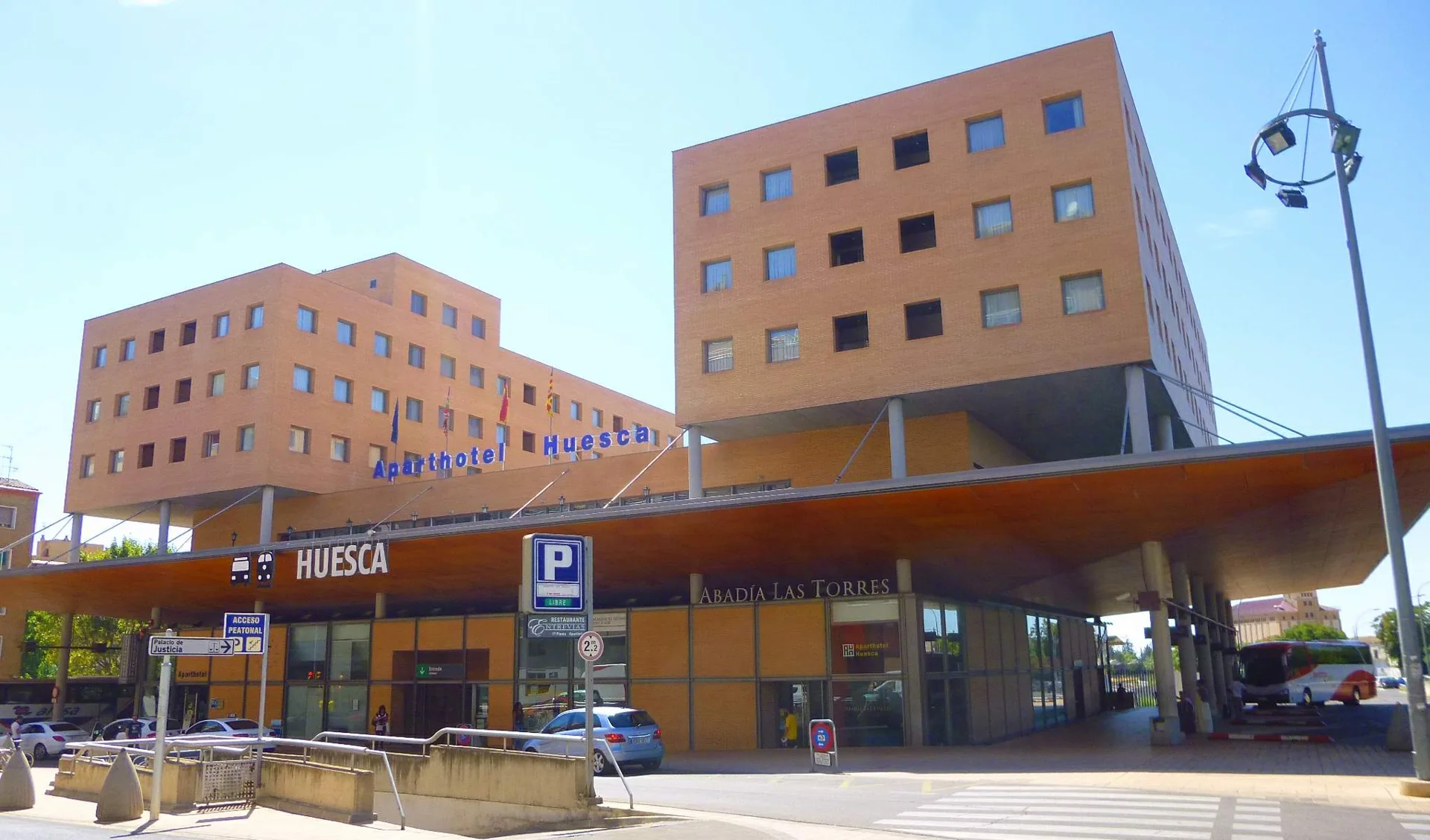 Fachada de la Estación Intermodal de Huesca con el rótulo de la ciudad bajo la marquesina y un autobús en las dársenas