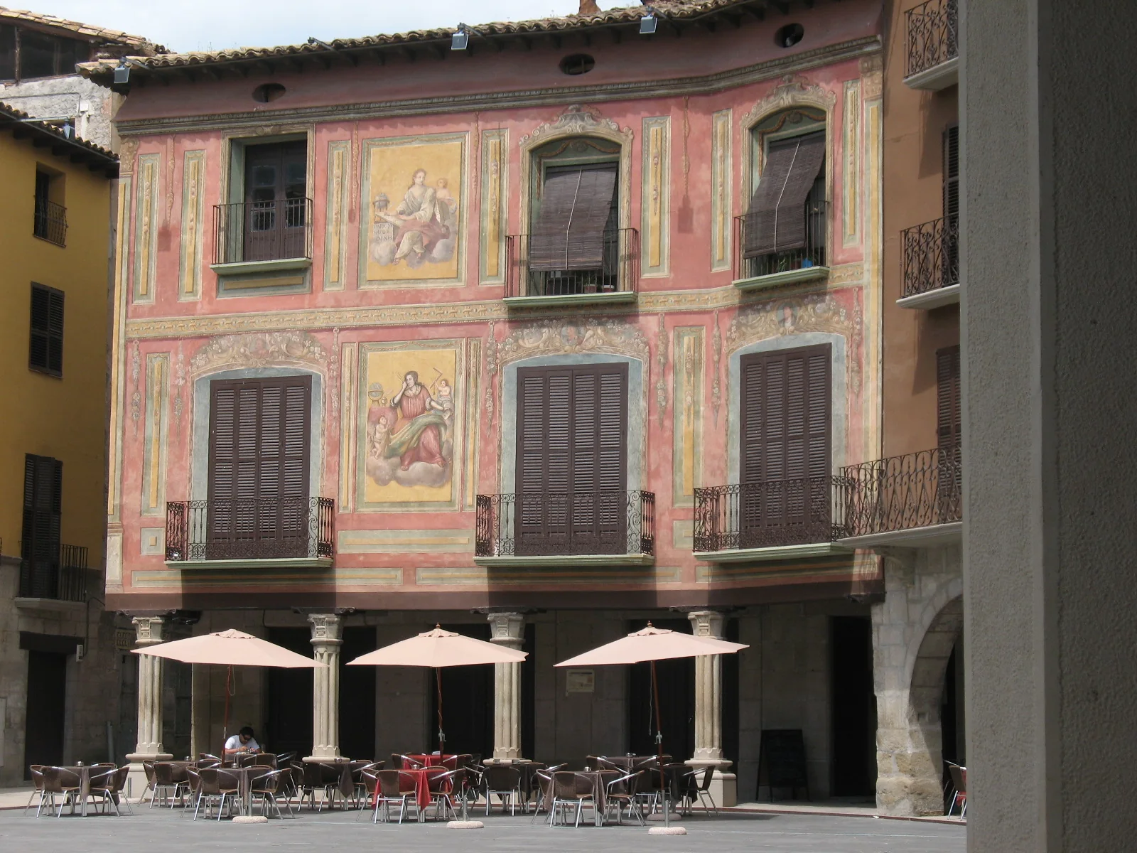 Plaza Mayor de Graus con edificio renacentista de fachada rosa decorado con frescos religiosos y terraza de bar en soportales