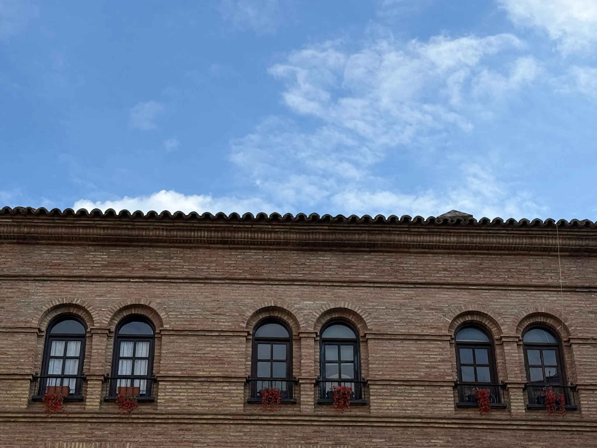 Fachada de ladrillo con ventanas de arco decoradas con flores rojas en el casco histórico de Huesca. Foto propia La Maleta Inquieta, octubre 2026