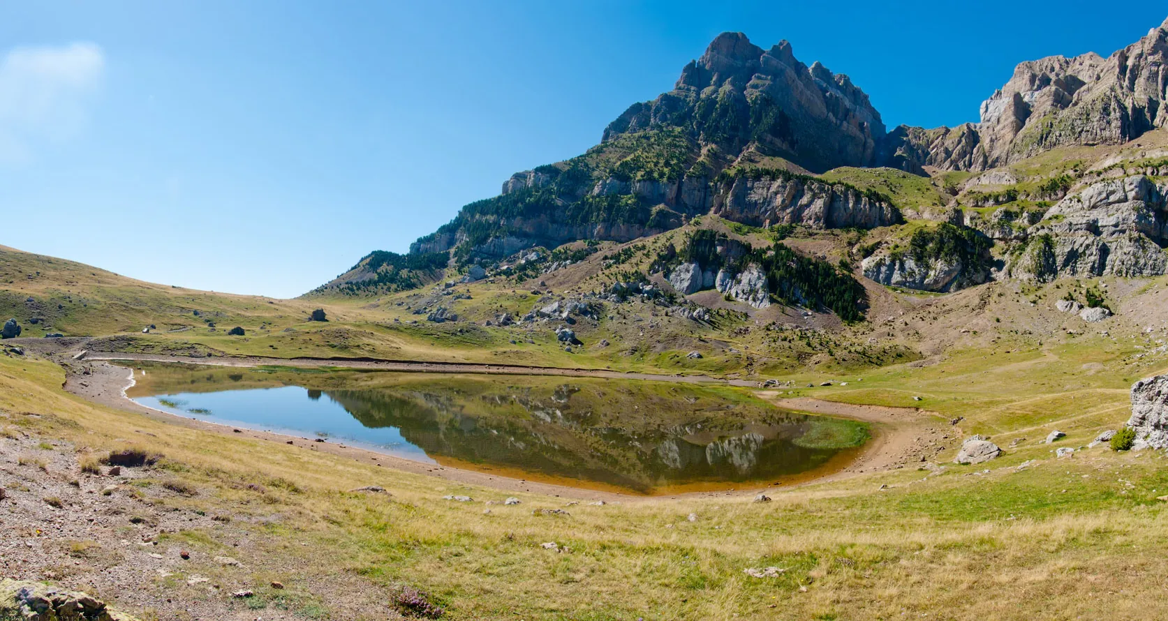 Ibón de Piedrafita, lago pequeño entre pastos de altura a los pies de las paredes calizas de Peña Telera, valle de Tena