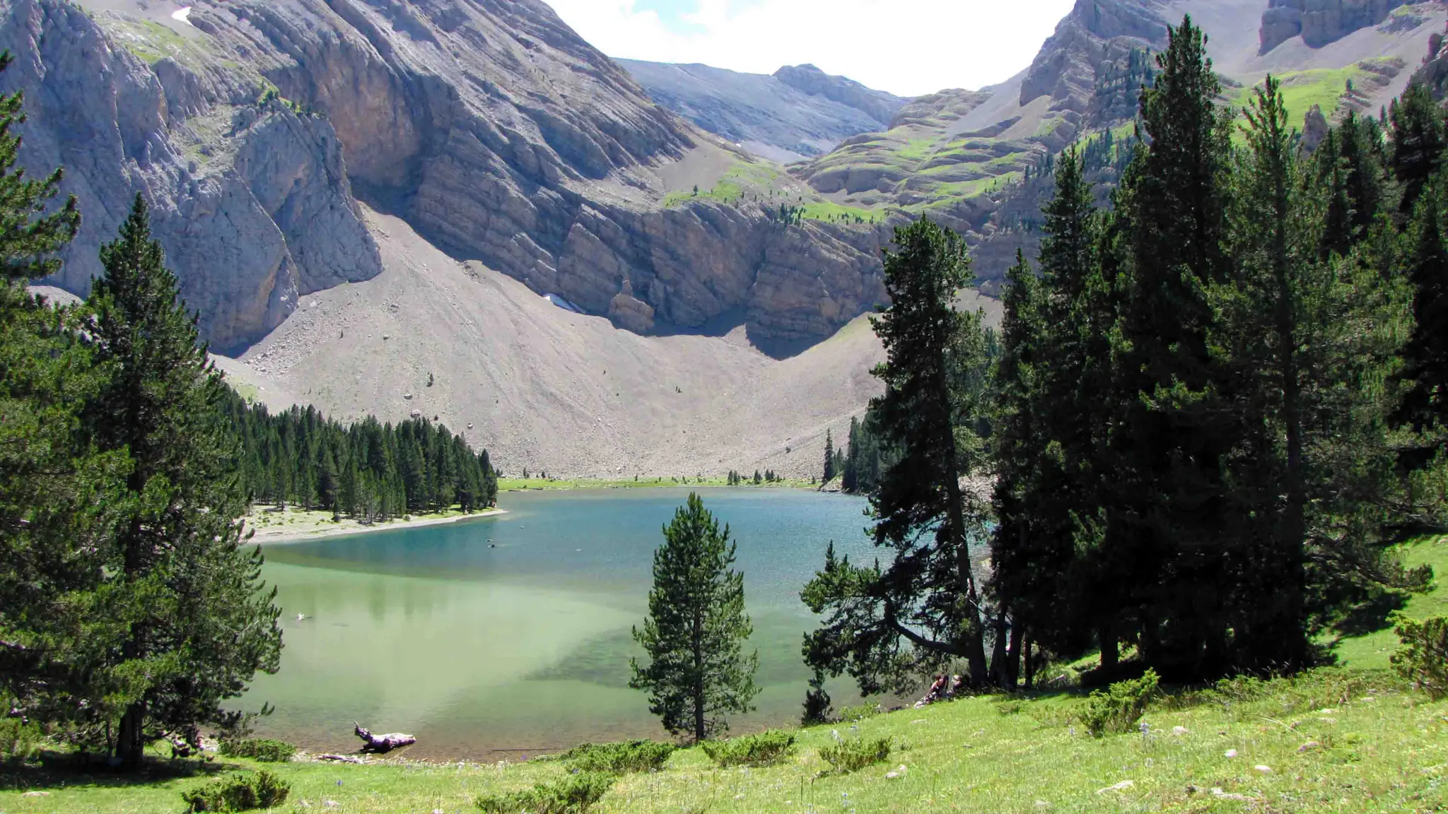 Ibón de Plan o Basa de la Mora, lago de aguas verdes rodeado de pinos bajo las paredes rocosas del macizo de Cotiella
