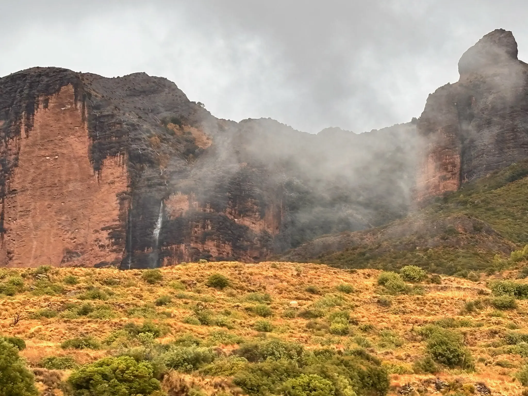 Pared vertical de los Mallos de Riglos con cascada estacional y estratos rojizos de conglomerado en niebla. Foto propia La Maleta Inquieta, octubre 2026