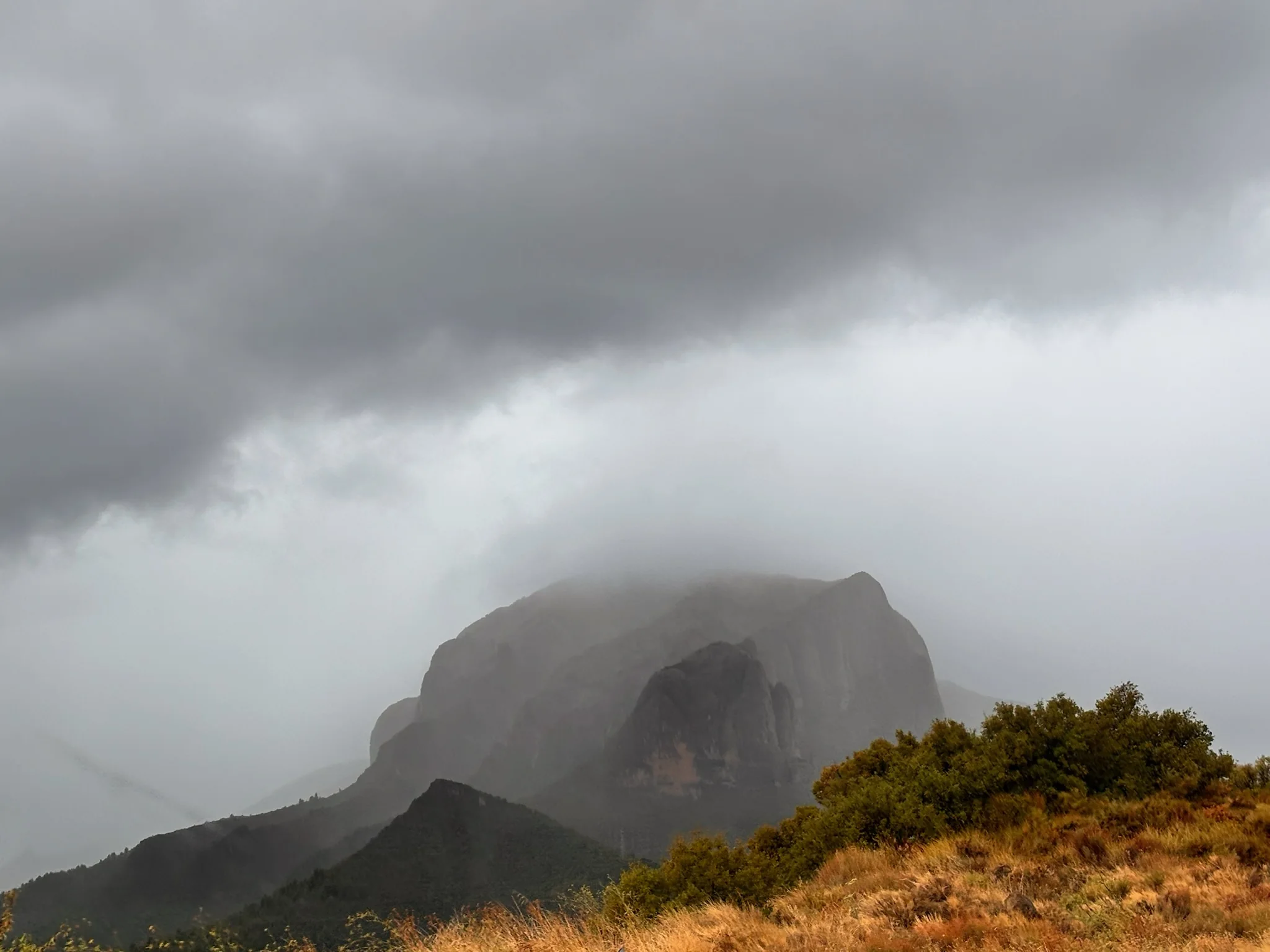 Mallo de Riglos envuelto en niebla densa visto desde ladera con vegetación otoñal bajo cielo gris. Foto propia La Maleta Inquieta, octubre 2026