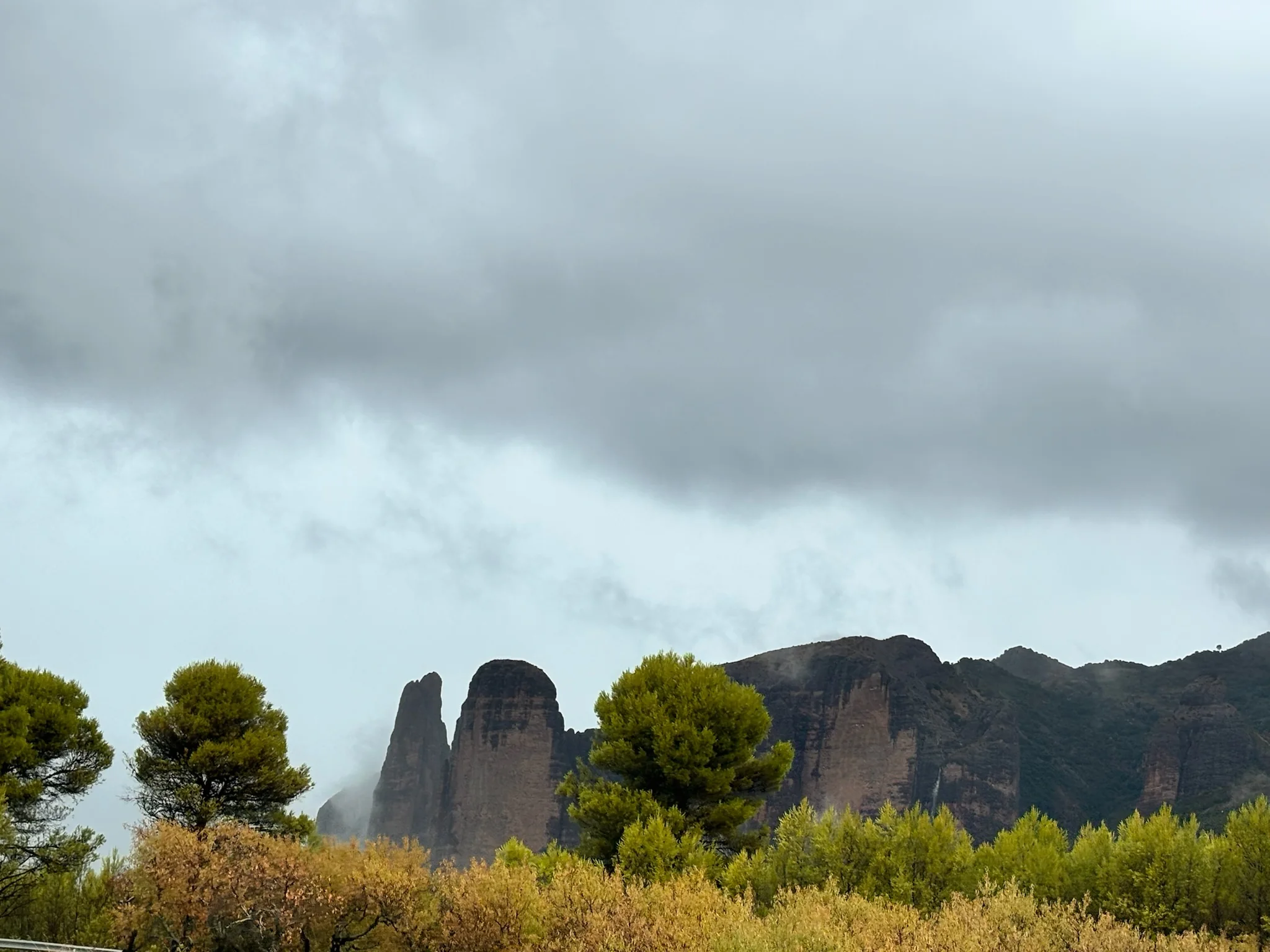 Mallos de Riglos entre la niebla, con pinos carrascos en primer plano y hierba seca otoñal. Foto propia La Maleta Inquieta, octubre 2026