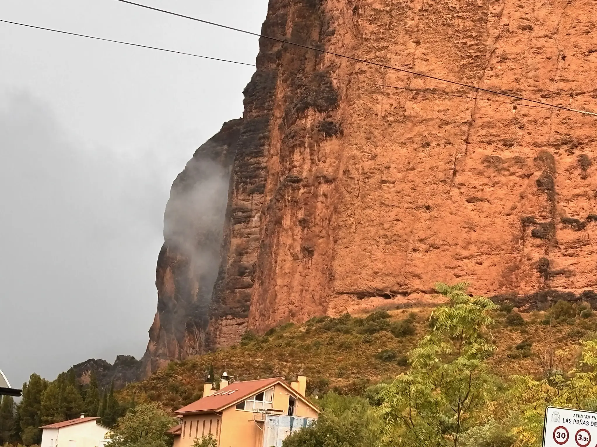 Pared vertical del Mallo de Riglos sobre el pueblo, con casa de tejado naranja y cables en primer plano. Foto propia La Maleta Inquieta, octubre 2026