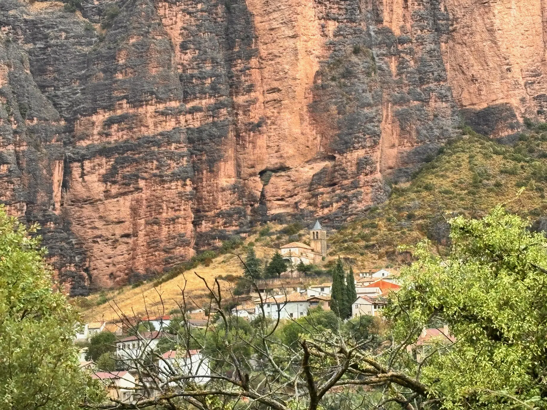 Pueblo de Riglos con iglesia románica y campanario bajo la pared vertical de los Mallos de conglomerado rojizo. Foto propia La Maleta Inquieta, octubre 2026