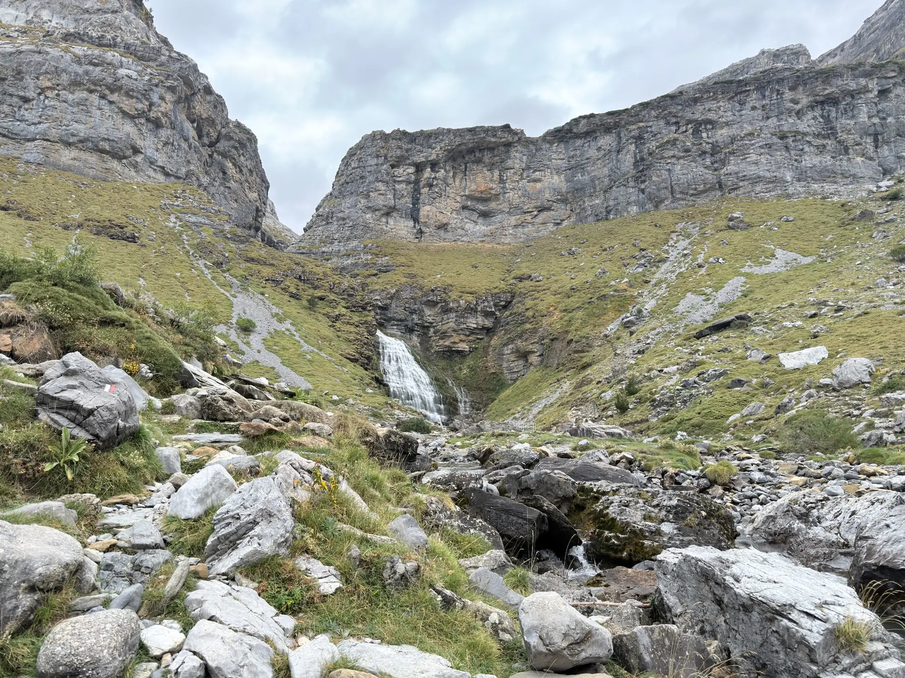 Cascada al fondo entre paredes rocosas con río Arazas y rocas en primer plano en el valle de Ordesa. Foto propia La Maleta Inquieta, octubre 2026