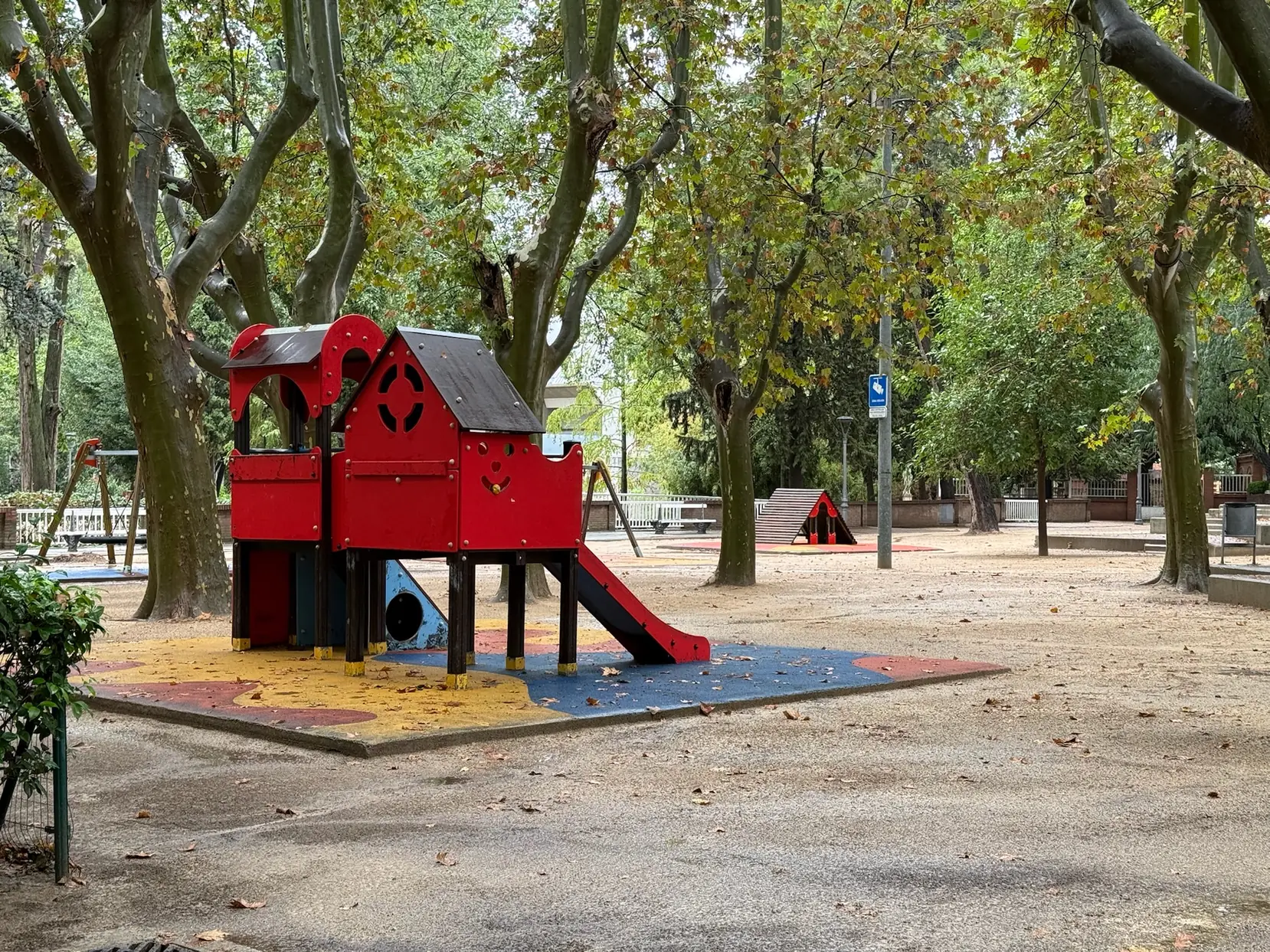 Parque infantil con estructura roja de tobogán y torre en el Parque Miguel Servet de Huesca rodeado de árboles. Foto propia La Maleta Inquieta, octubre 2026