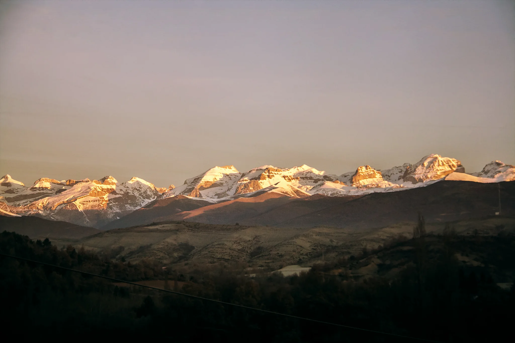 Cordillera del Pirineo con cumbres nevadas iluminadas por la luz rosada del atardecer sobre paisaje oscuro