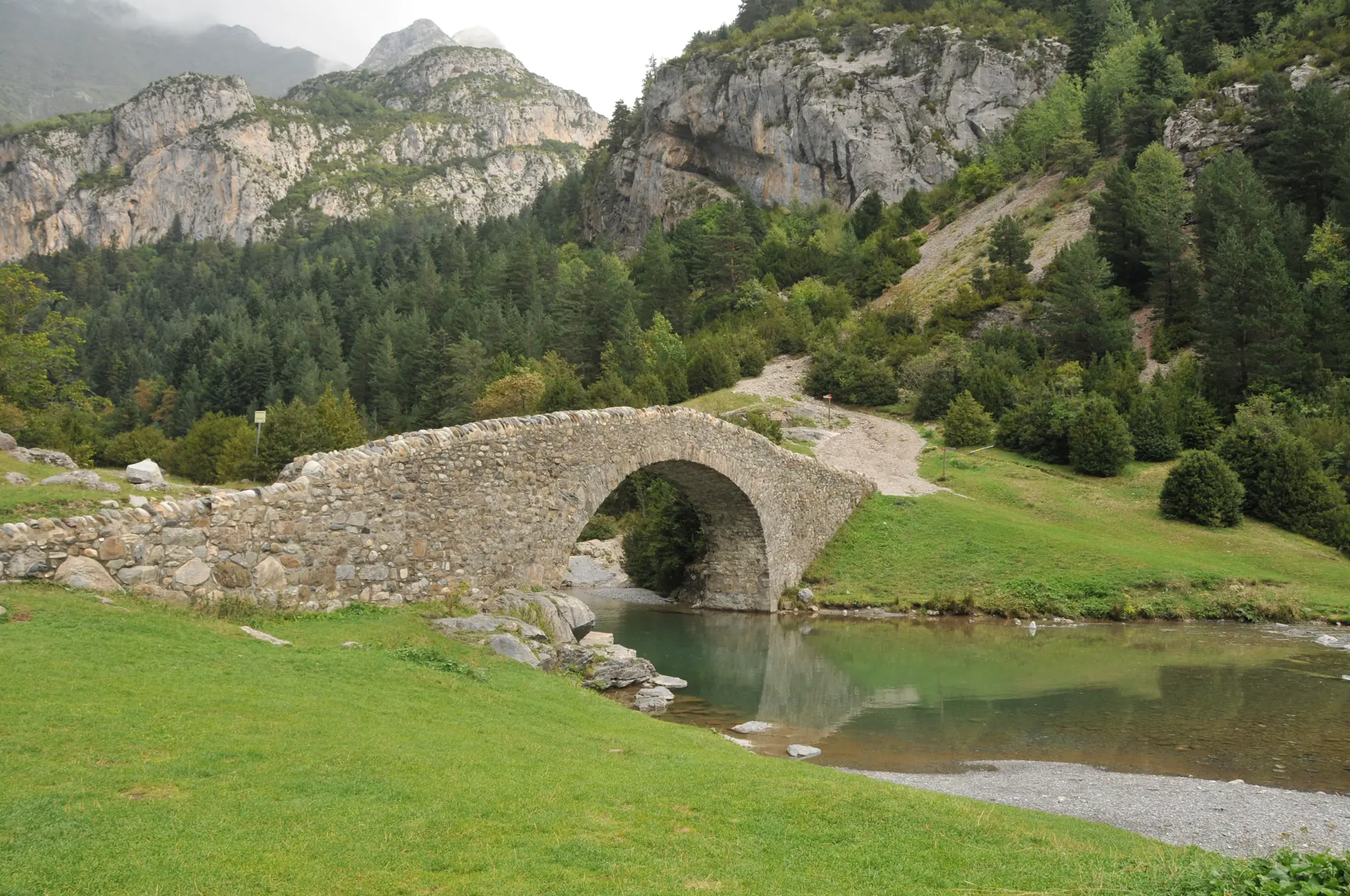 Puente medieval de piedra de San Nicolás de Bujaruelo sobre el río con paredes rocosas verticales y bosques al fondo