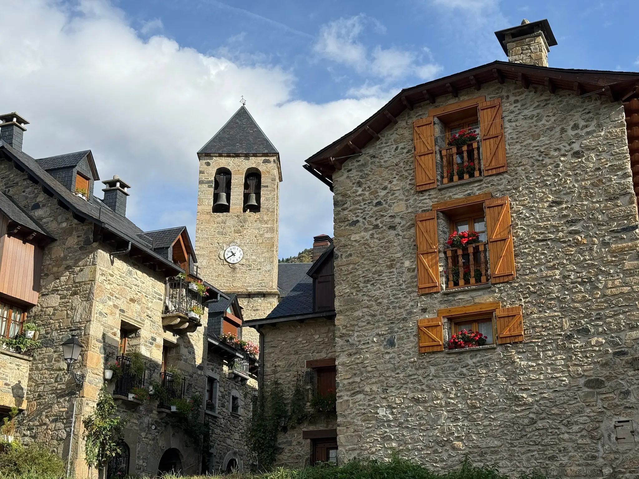Casas de piedra con contraventanas naranjas y geranios y la torre campanario al fondo en Sallent de Gállego. Foto propia La Maleta Inquieta, octubre 2026