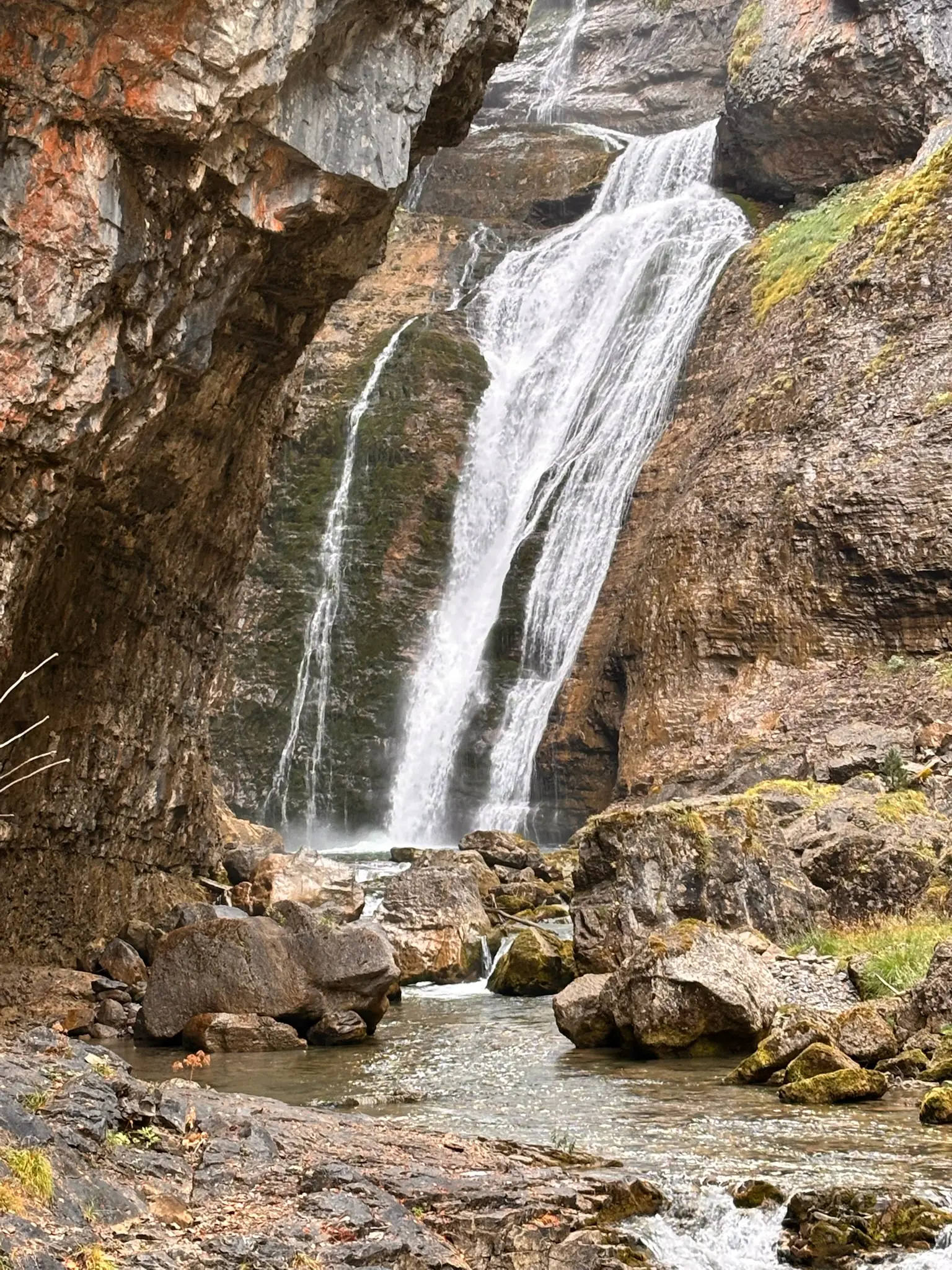 Salto de agua entre paredes verticales de roca caliza cubiertas de musgo verde, con poza y rocas al pie. Foto propia La Maleta Inquieta, octubre 2026