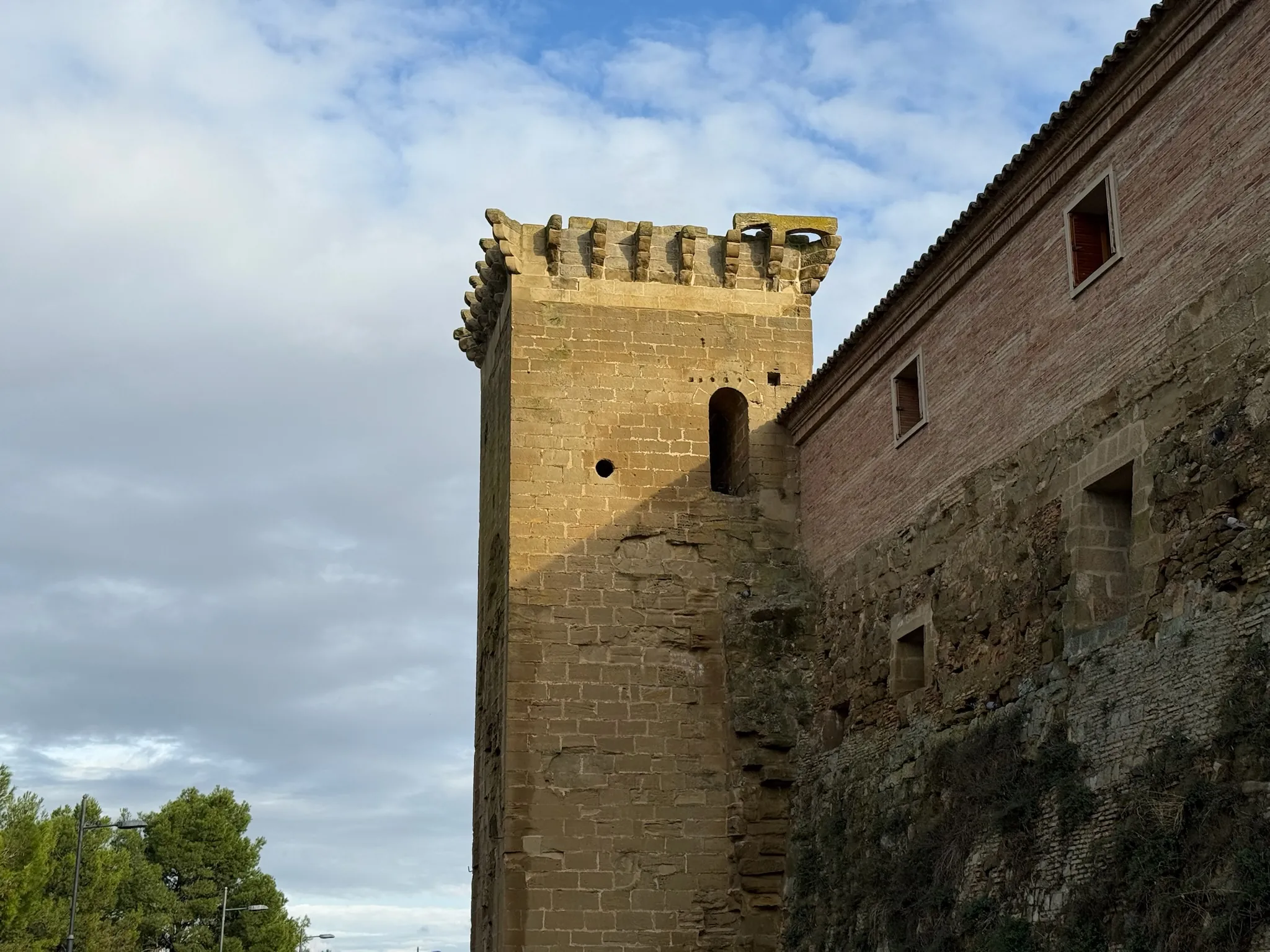 Torreón de piedra con almenas de la muralla de Huesca junto a un edificio de ladrillo levantado sobre el lienzo. Foto propia La Maleta Inquieta, octubre 2026