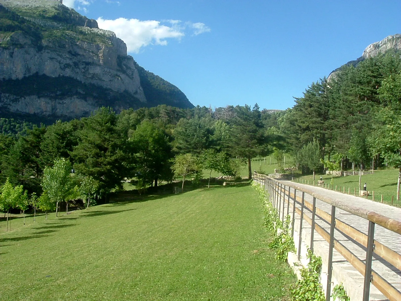 Valle de Hecho con prados verdes intensos rodeados de paredes rocosas y bosques de coníferas bajo cielo azul con nubes